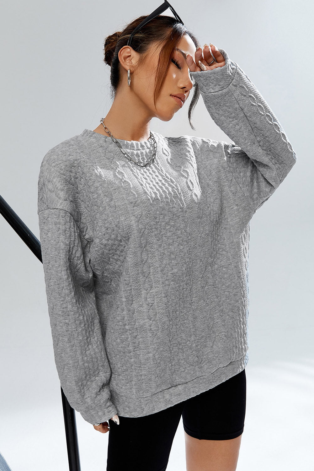 Sivi pulover s kabelskom teksturom na spuštena ramena